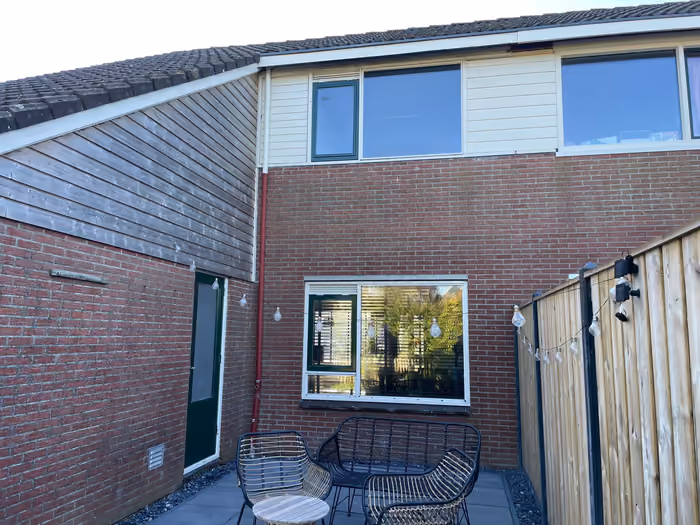 Achtergevel met nieuwe donkergroene kozijnen, terras met tuinstoelen en houten schutting