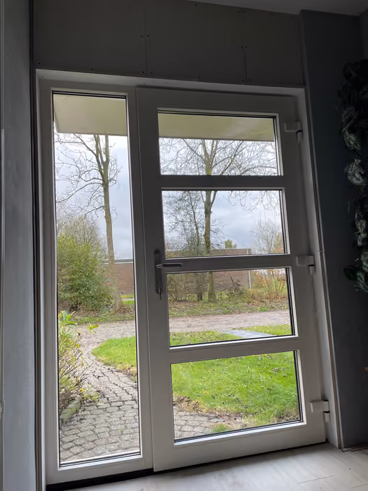 Nieuwe witte buitendeur met zijlicht van binnenuit, wanden nog onafgewerkt