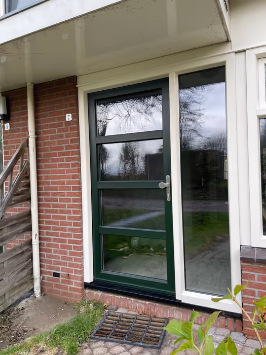 Donkergroene buitendeur met glasvlakken en wit zijlicht onder een luifel