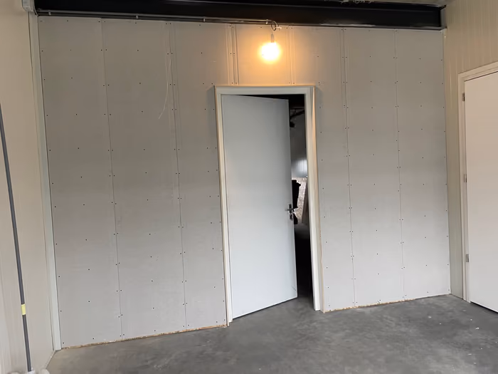 Wand met gipsplaten en geplaatste binnendeur op een betonvloer