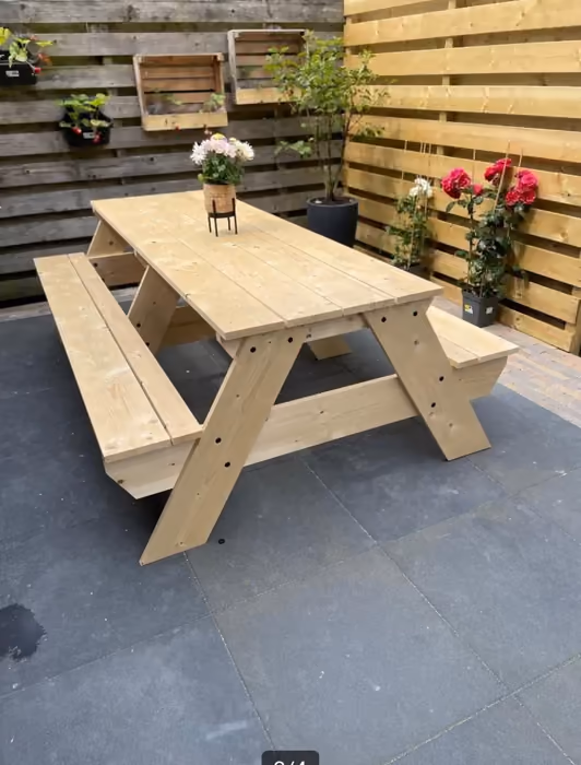 Houten picknicktafel op tegels voor een schutting met plantenbakken en rozen