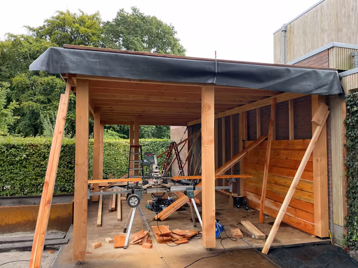Houten overkapping in aanbouw met dakfolie, verstekzaag en gestapeld hout