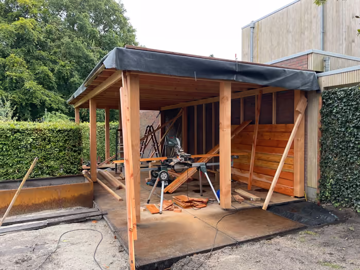 Constructie van een houten overkapping met zwarte dakfolie en schoren