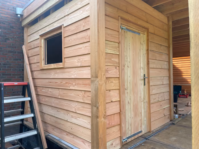 Houten wand met rabatdelen, klein raampje en nieuwe houten deur