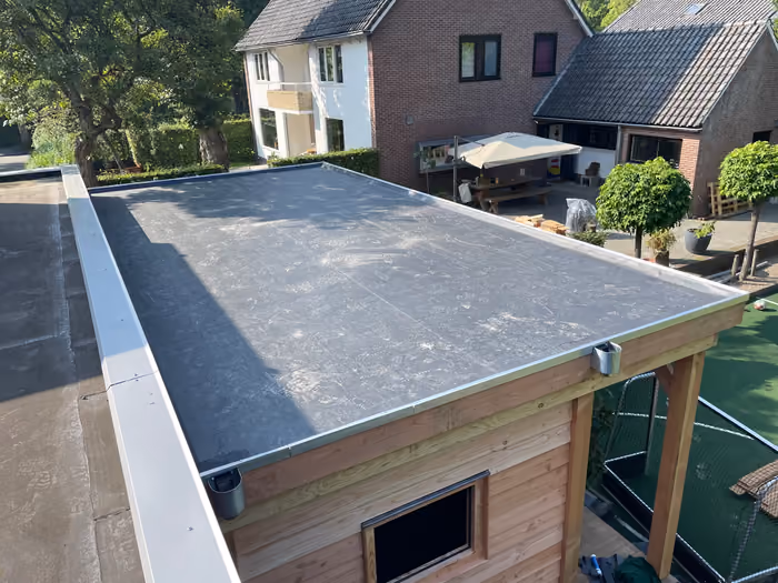 Afgewerkt EPDM-dak met metalen daktrim en twee spuwers boven een houten berging