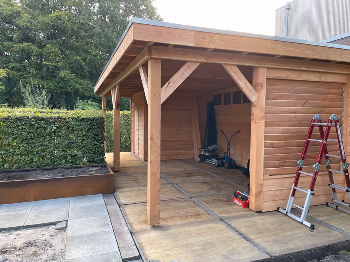 Houten berging met aangebouwde overkapping en houten vlonder in de tuin