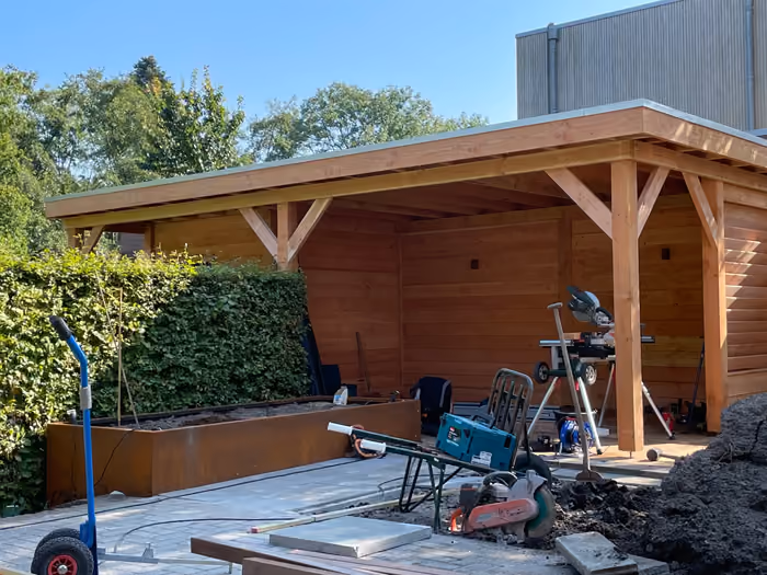 Overkapping met plat dak in aanbouw, gereedschap en zand in de tuin