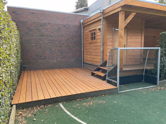 Hardhouten vlonder met traptrede naast een houten berging met raampje
