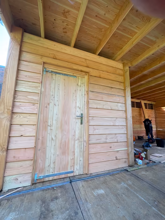 Houten deur in de gevel van de berging onder de overkapping