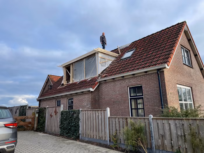 Dakkapel in aanbouw op een pannendak, man staat bovenop het dak