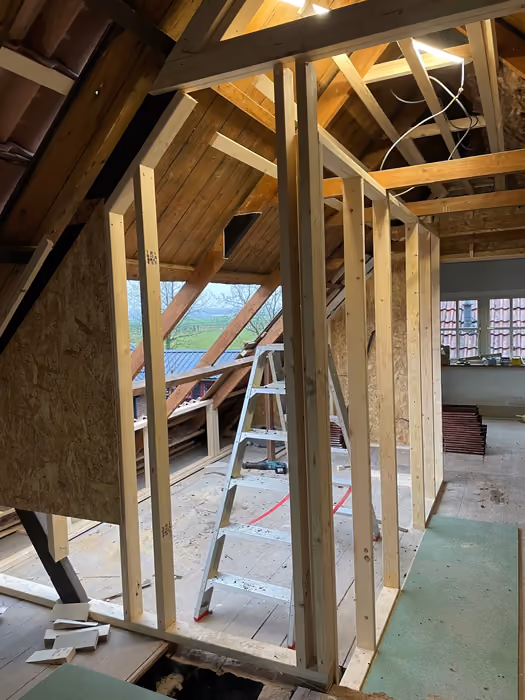 Zolder met houten regelwerk en trapje, uitzicht door de open dakkapel