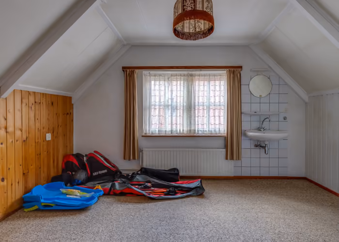Zolderkamer met schuin plafond, wastafel en raam met gordijnen