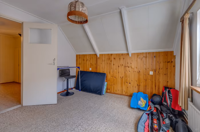 Zolderkamer met houten lambrisering en witte schuine wanden