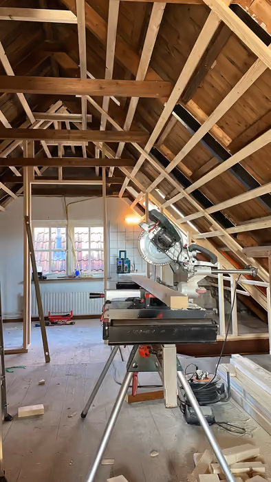 Zolder met open kapconstructie en verstekzaag op een werkbank