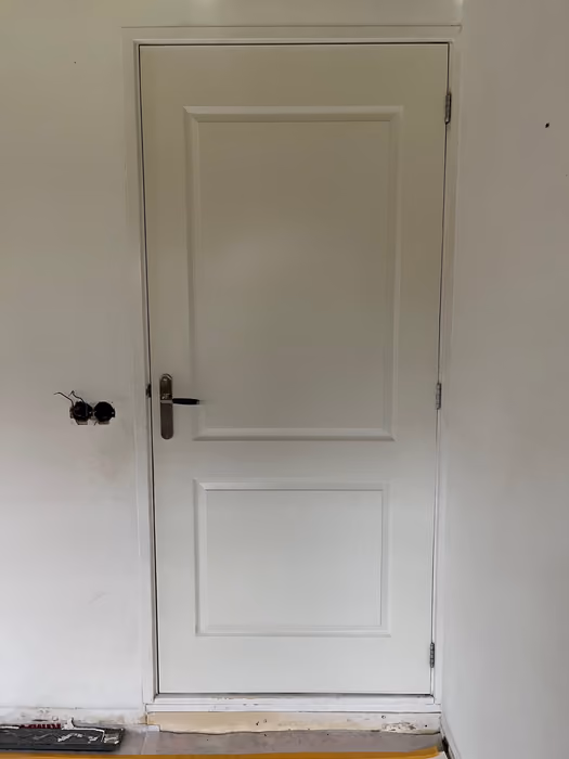 Nieuwe witte paneeldeur in kozijn tegen een nog onafgewerkte wand