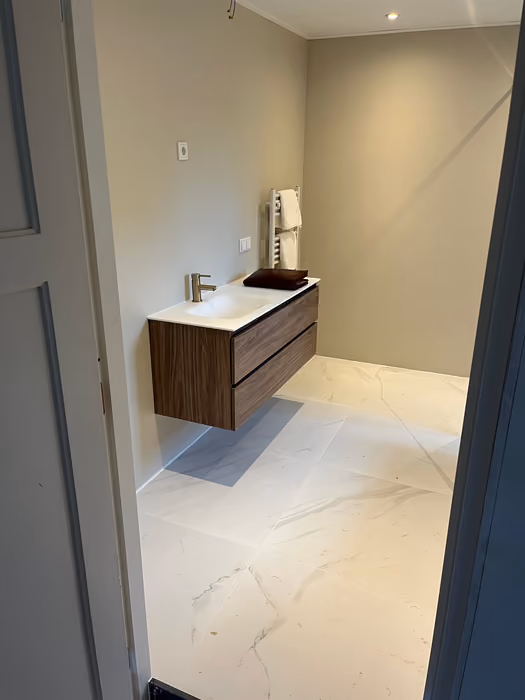 Badkamer met zwevend houten wastafelmeubel en lichte tegelvloer met marmermotief
