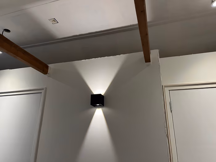 Afgewerkt plafond met zichtbare balken en zwarte wandlamp in een hoek