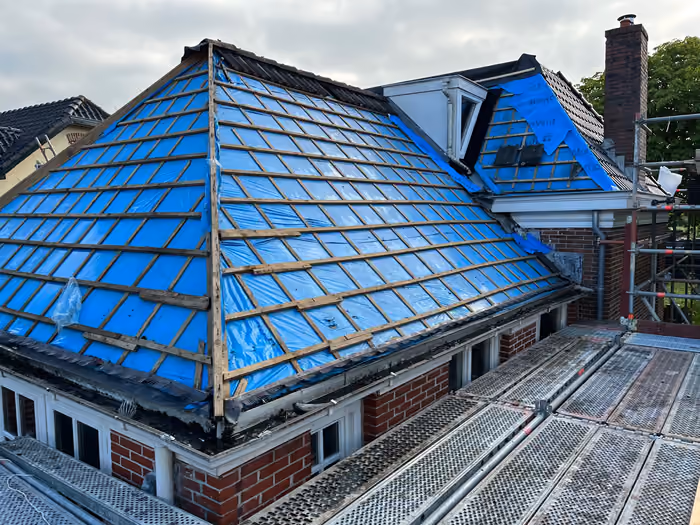 Dak gestript tot de panlatten met blauwe folie eronder en steigerdek ernaast