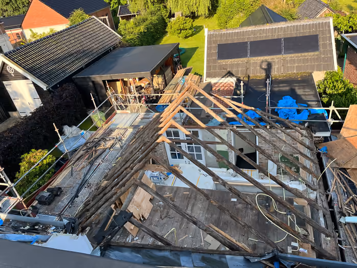 Dak van bovenaf met blootgelegde spanten en steigers rond de woning