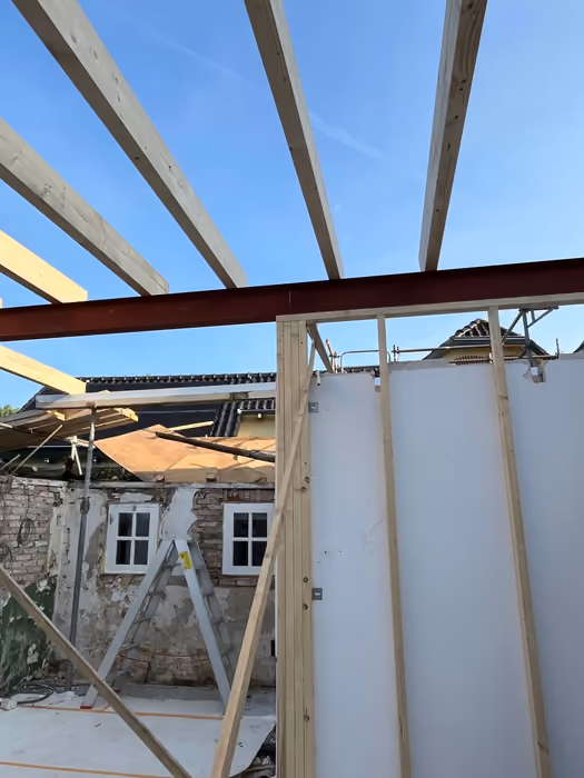 Houten dakbalken rusten op een stalen ligger boven een nieuwe aanbouw