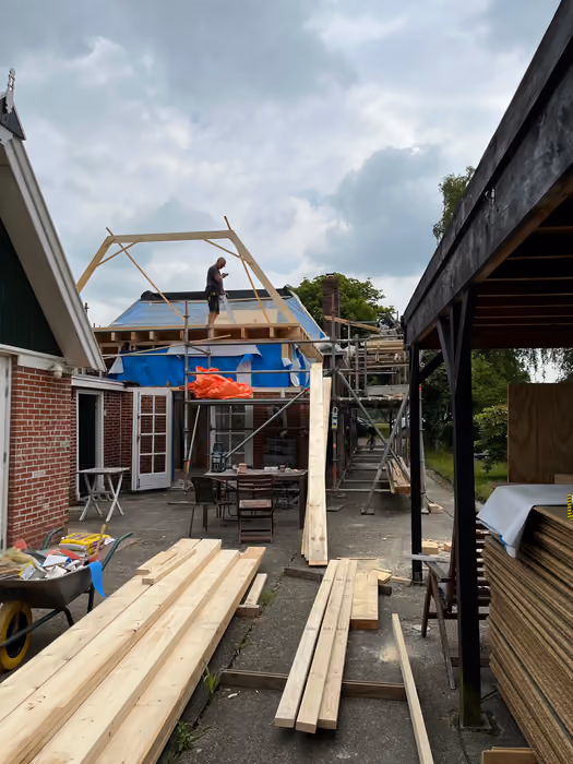 Timmerman op de steiger bij een nieuwe kapconstructie, stapels hout op terras