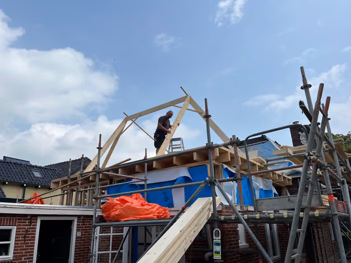 Timmerman zet een houten spant vast op de steiger van de kapconstructie