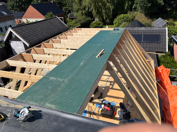 Nieuwe kap met houten sporen en groene dakplaten, gezien vanaf het buurdak