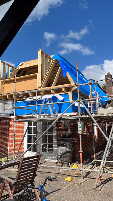Houten opbouw van dakkapel met steiger en blauwe dakfolie tegen blauwe lucht